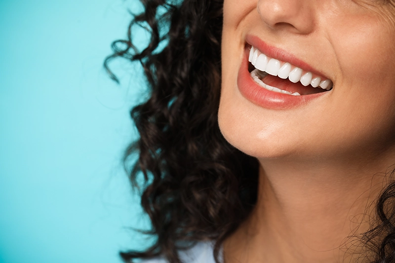 Blue background, woman smiling with just bottom of face and neck in frame.